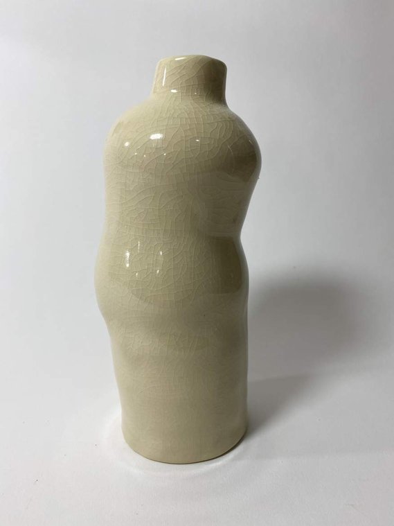 a vase that resembles a body leaning over, possibly having abdominal pain. it is glazed in a glossy off-white crackled glaze