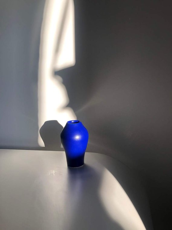  a small bright blue vase sits on a white table with many shadows casting from natural light