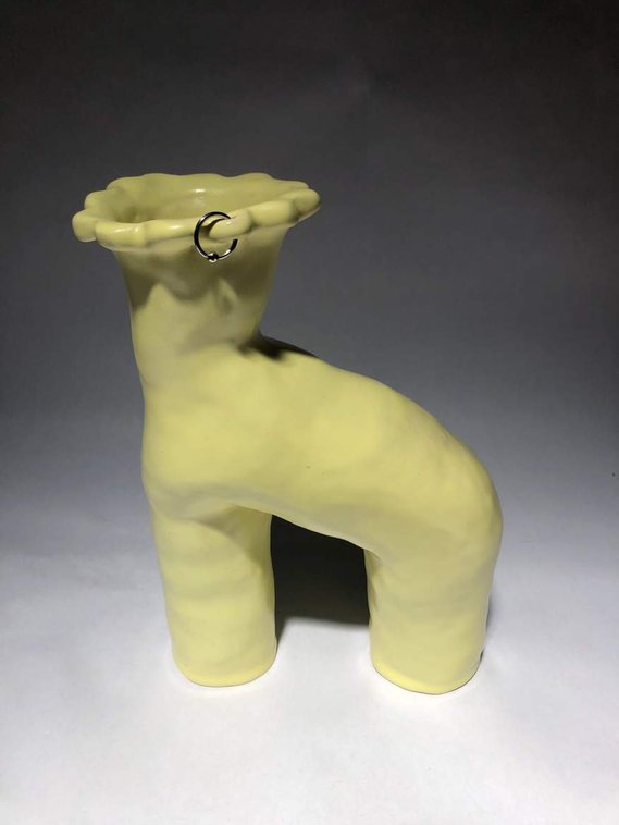 a pastel yellow vessel that has a hoop earing pierced through one of the floral looking petals