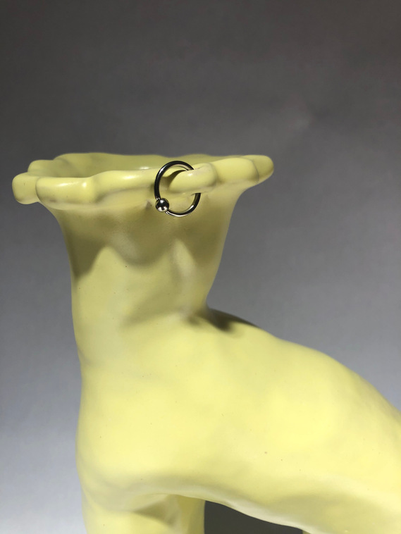 a pastel yellow vessel that has a hoop earing pierced through one of the floral looking petals
