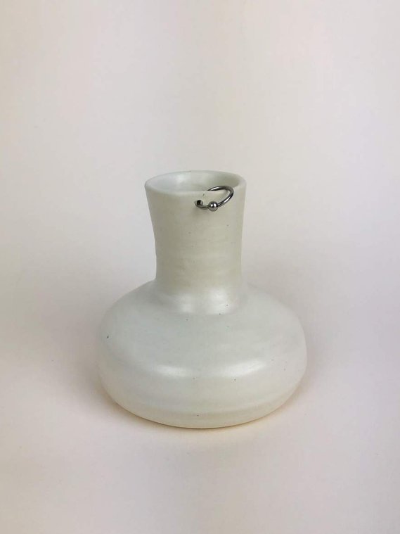 a wide and short carafe in a marshmallow glaze with a silver hoop piercing through the top of the stem