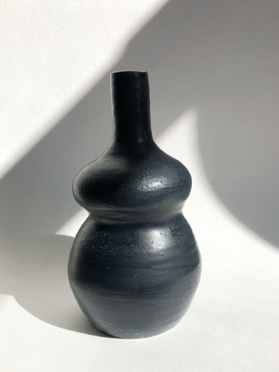  a black vase that has two tiers-- the top tier (after the stem) is much thinner than the bottom tier. it resembles a woman in an abstract way.
