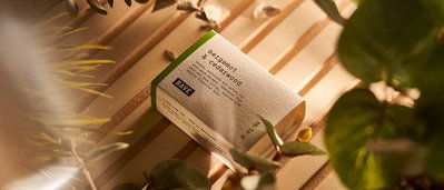 Bergamot and Cedarwood skincare soap, placed on a light wooden backdrop, photographed through the greenery and foliage.