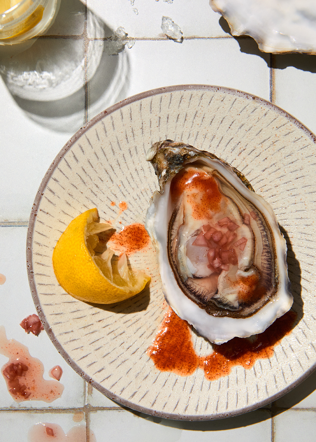 Fresh oysters with spicy red onion dressing on a sun drenched tiled surface. Delicious food photography by south east London based tableware photographer Lol Johnson. Food prep and styling by Iona Blackshaw and prop styling by Nuala Sharkey.