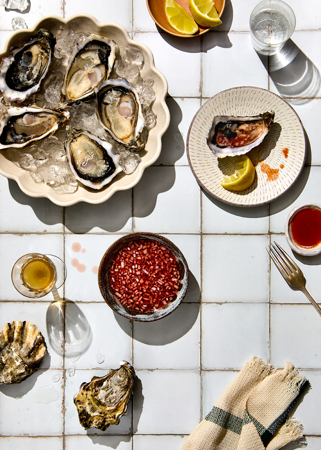 Fresh oysters with spicy red onion dressing on a sun drenched tiled surface. Delicious food photography by south east London based tableware photographer Lol Johnson. Food prep and styling by Iona Blackshaw and prop styling by Nuala Sharkey.