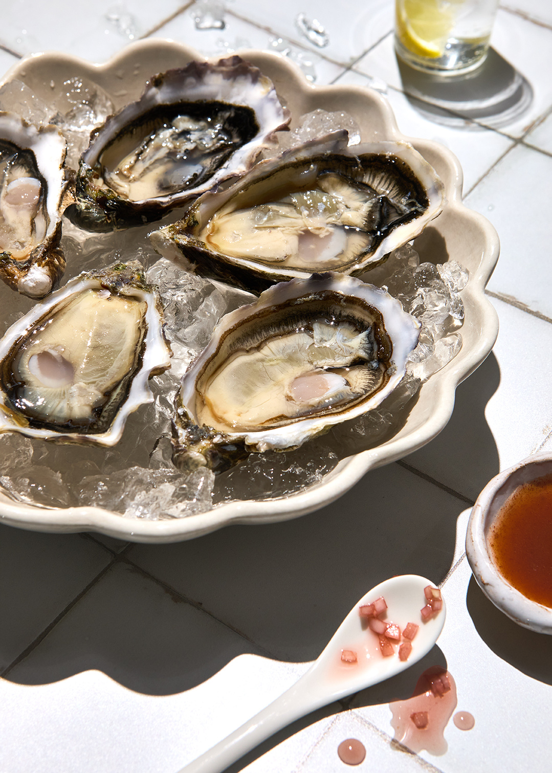 Fresh oysters with spicy red onion dressing on a sun drenched tiled surface. Delicious food photography by south east London based tableware photographer Lol Johnson. Food prep and styling by Iona Blackshaw and prop styling by Nuala Sharkey.