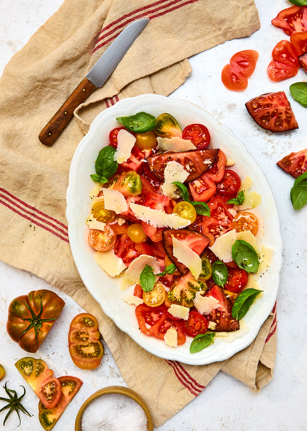 Soft, even light and shadows on a rustic surface.A dish featuring tomatoes, basil and parmesan and olive oil. Set upon a bistro napkin. Photography by Lol Johnson. Food prep and styling by Iona Blackshaw. Props by Nuala Sharkey.