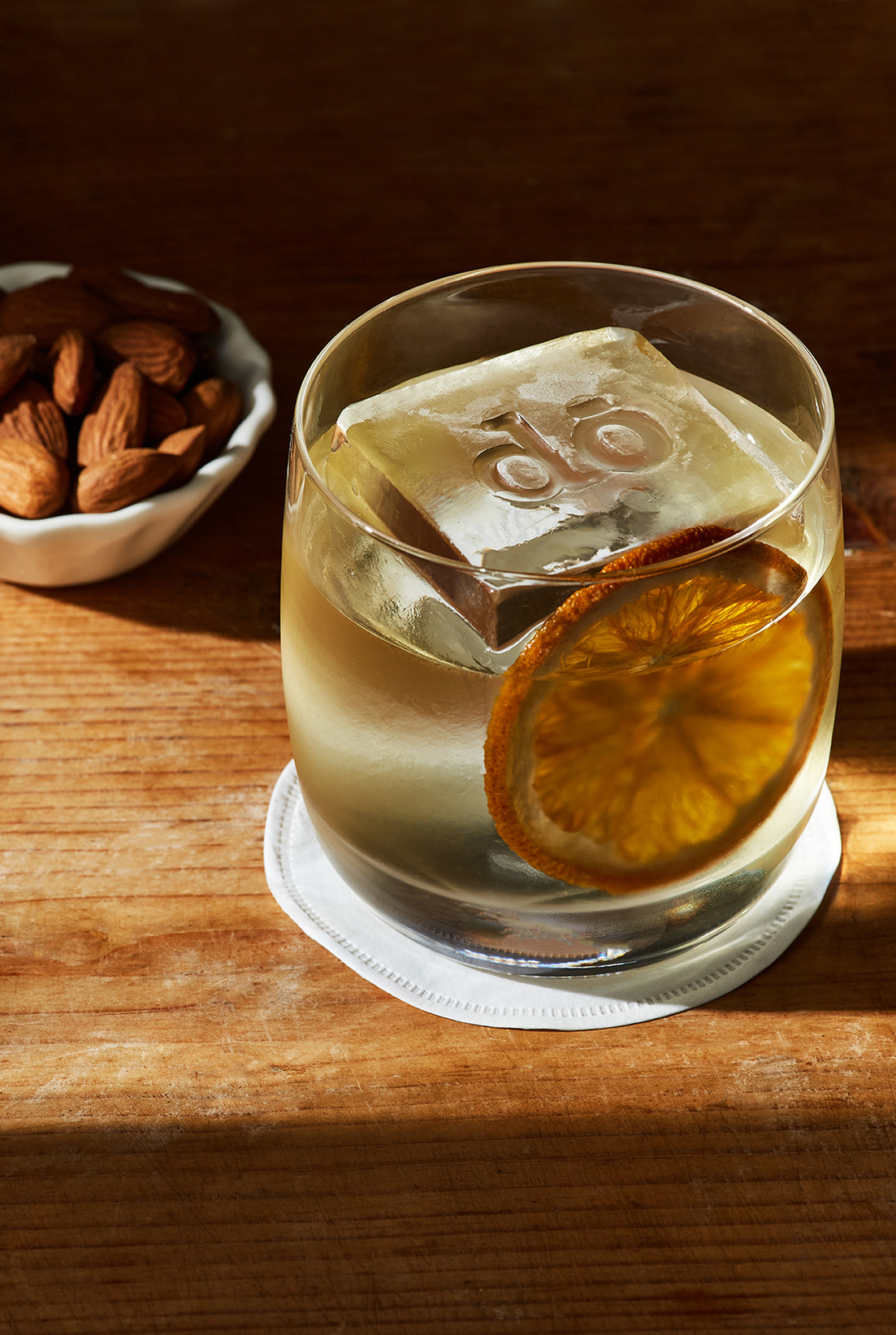 A white Negroni with  large branded icecube by Do Deli @ Hilton. Served with a side of salted Catalan almonds. Photography by London based food and drink photographer Lol Johnson. Drink prep and styling by Iona Blackshaw.