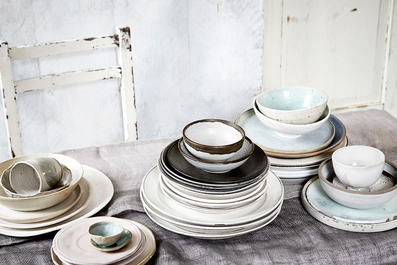Still life imagery of a range of ceramics and crockery shot on a muted tablecloth in front of a worn wooden chair from Topham Street props house. Shot for branding agency Seeing Things Creative by London based food and tableware photographer Lol Johnson.