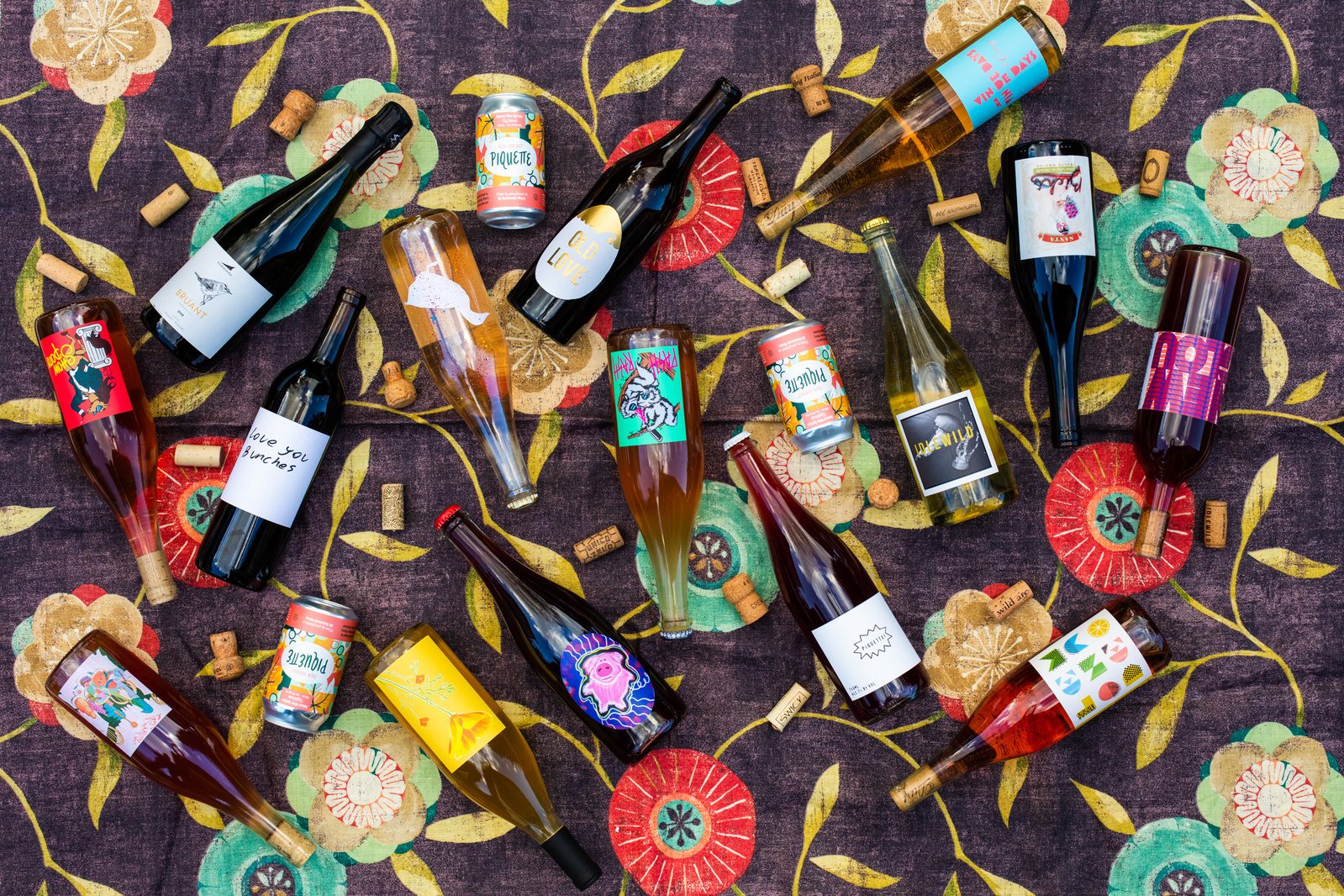 Overhead view of natural wine bottles scattered on a colorful fabric. 