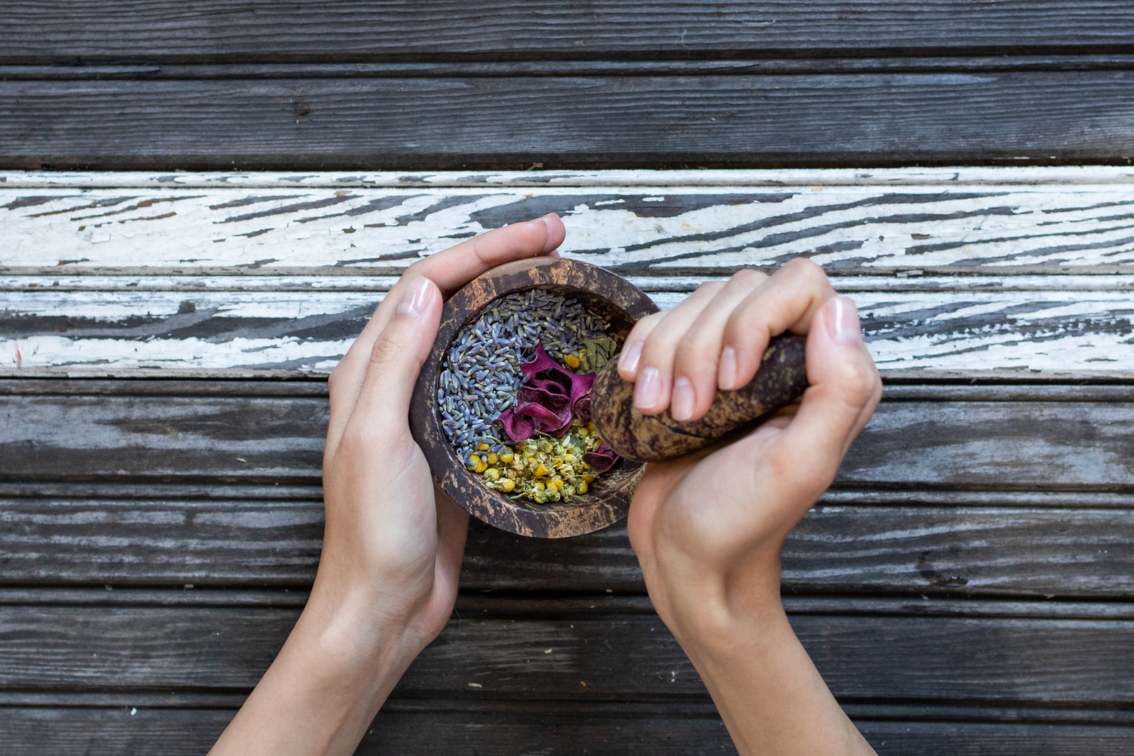 Branding photography of hands mixing lavender, chamomile and rose petals using a mortar and pestle. 