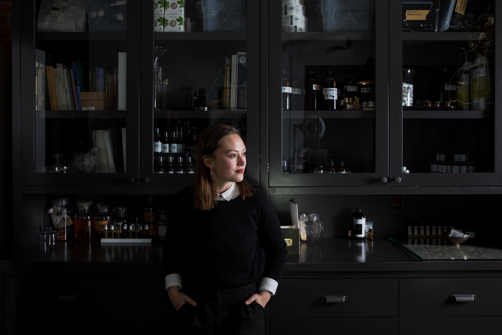 A woman standing in front of a dark apothecary cabinet. 