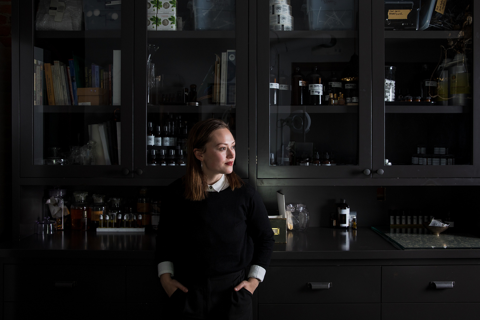A woman standing in front of a dark apothecary cabinet. 