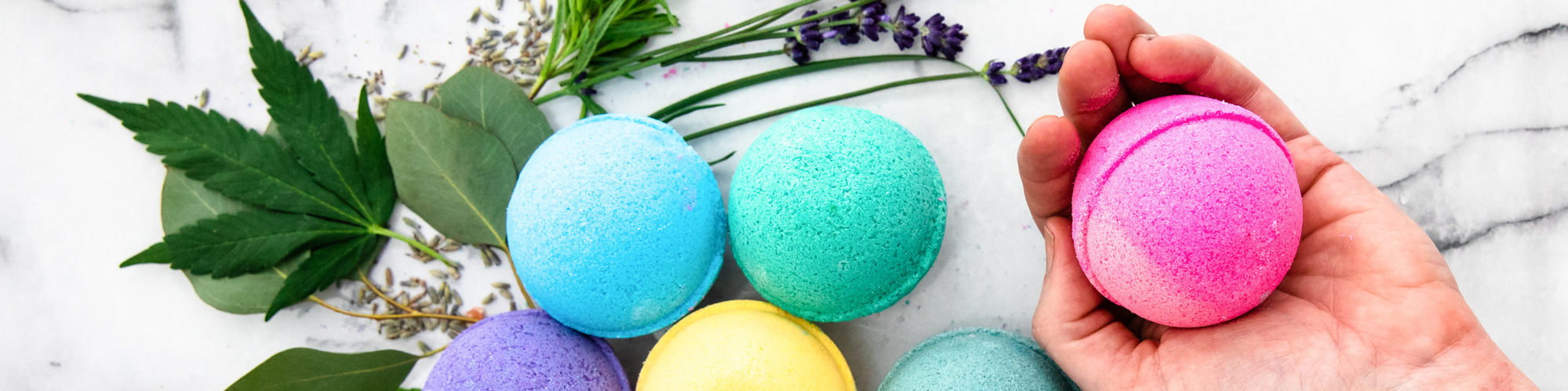Colorful CBD infused bathbombs, a hand holds a pink bath bomb. 
