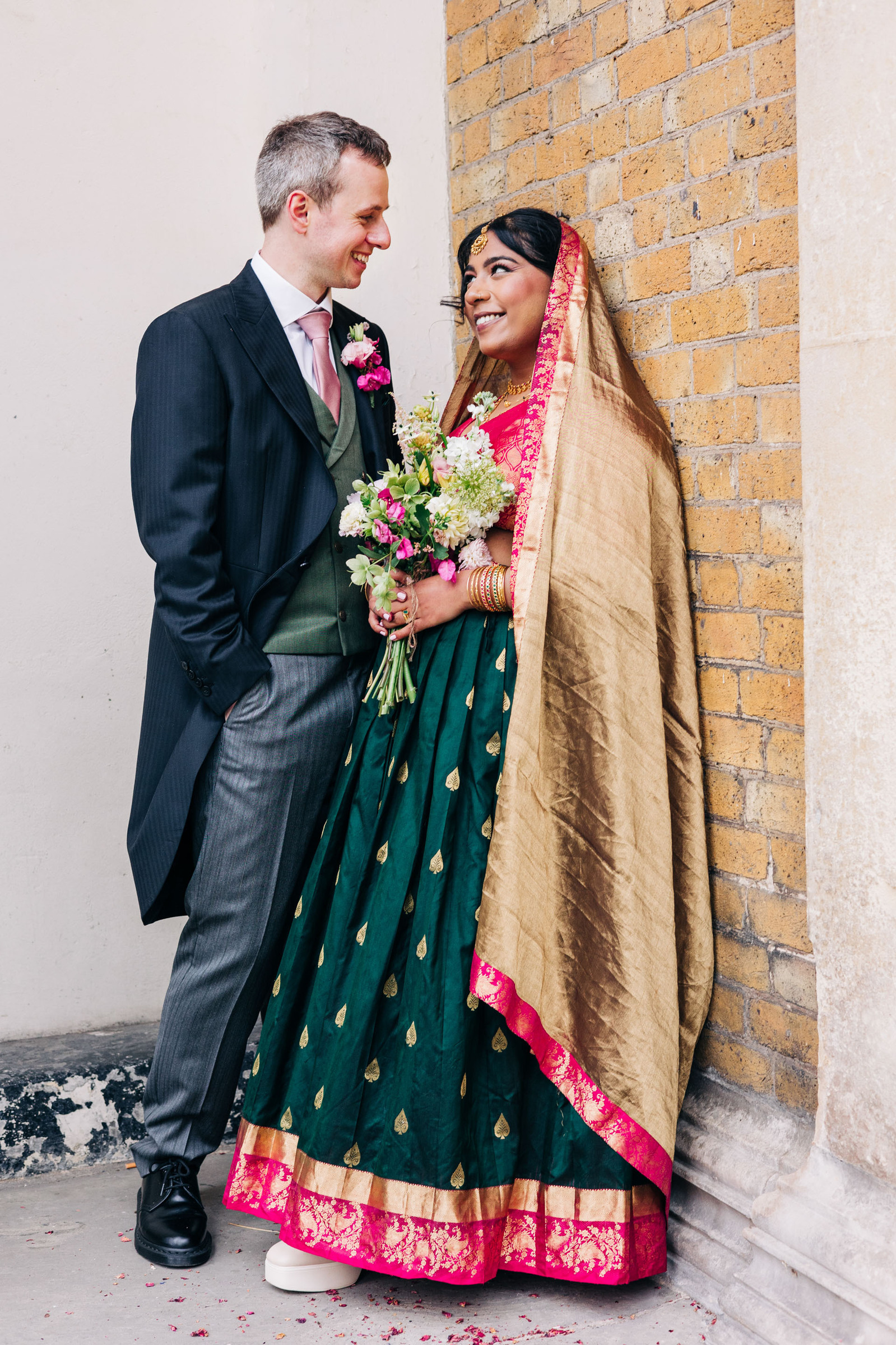 colorful multicultural british indian wedding at asylum chapel in london england UK wedding bride wearing hot pink and emerald green sari from nalli silks groom wearing suit from moss bros