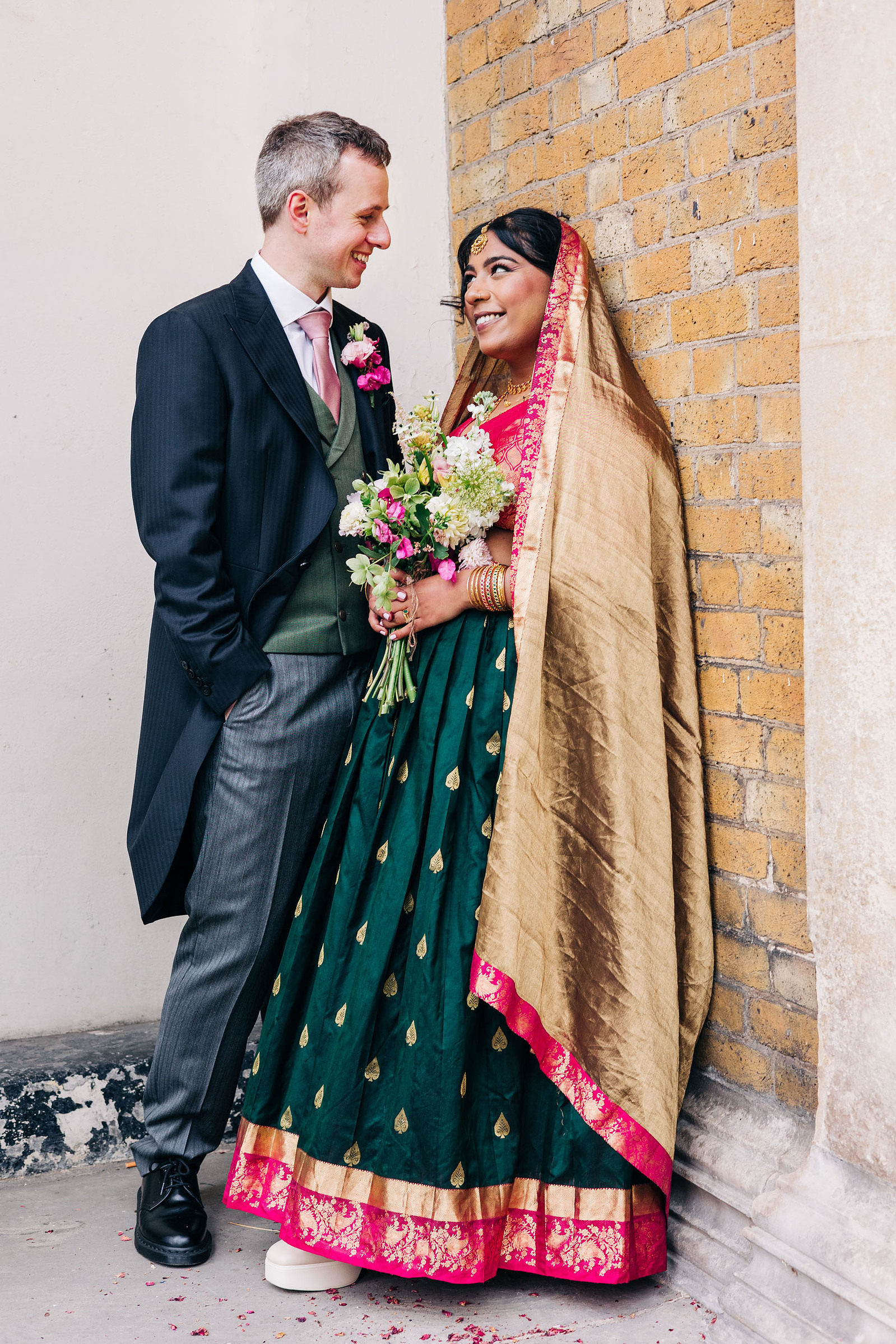 colorful multicultural british indian wedding at asylum chapel in london england UK wedding bride wearing hot pink and emerald green sari from nalli silks groom wearing suit from moss bros