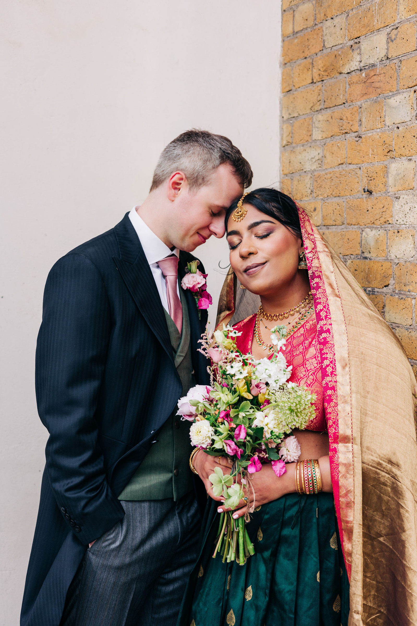 colorful multicultural british indian wedding at asylum chapel in london england UK wedding bride wearing hot pink and emerald green sari from nalli silks groom wearing suit from moss bros