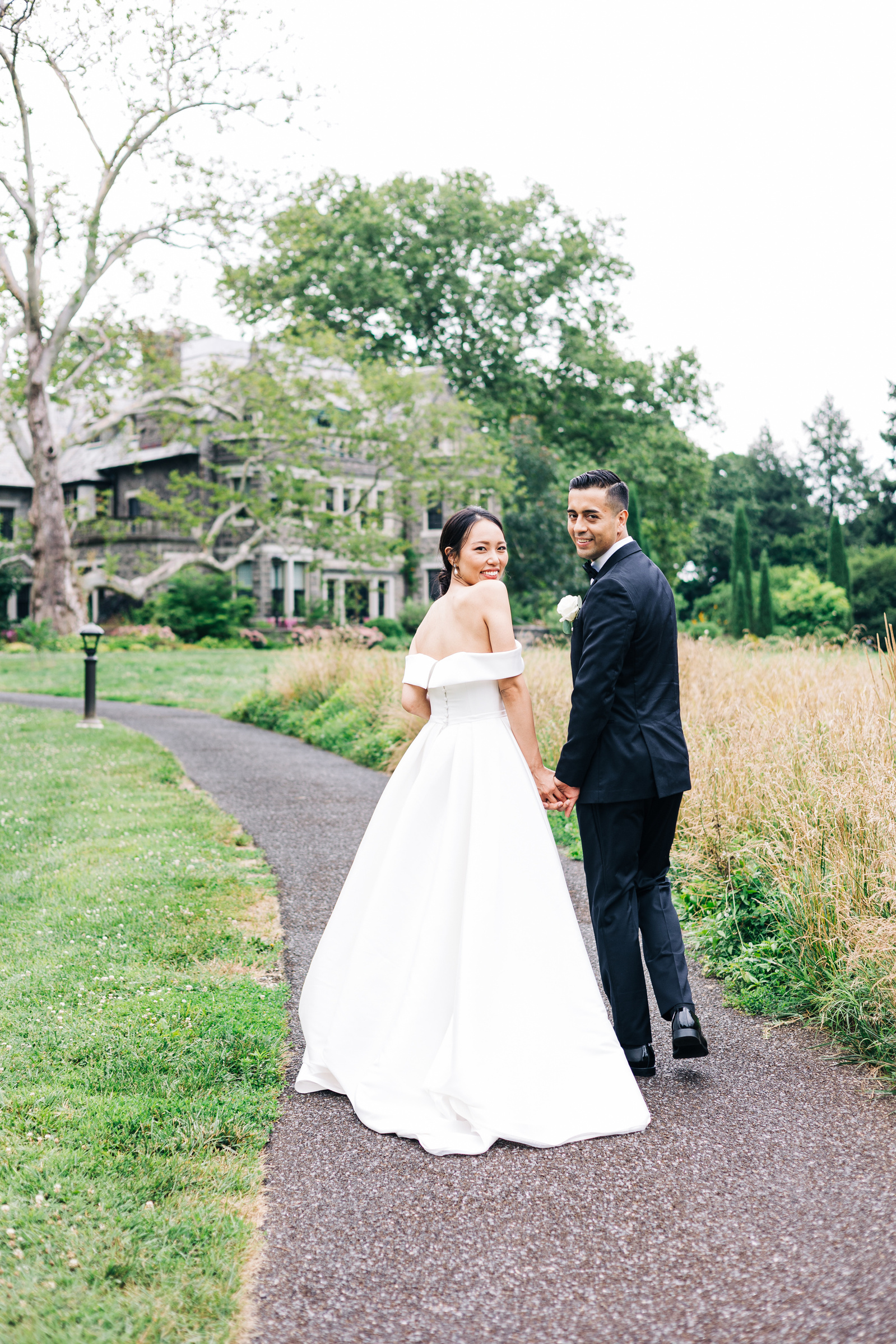 bride and groom walking down a path at stoneleigh gardens near philadelphia with stone mansion in background