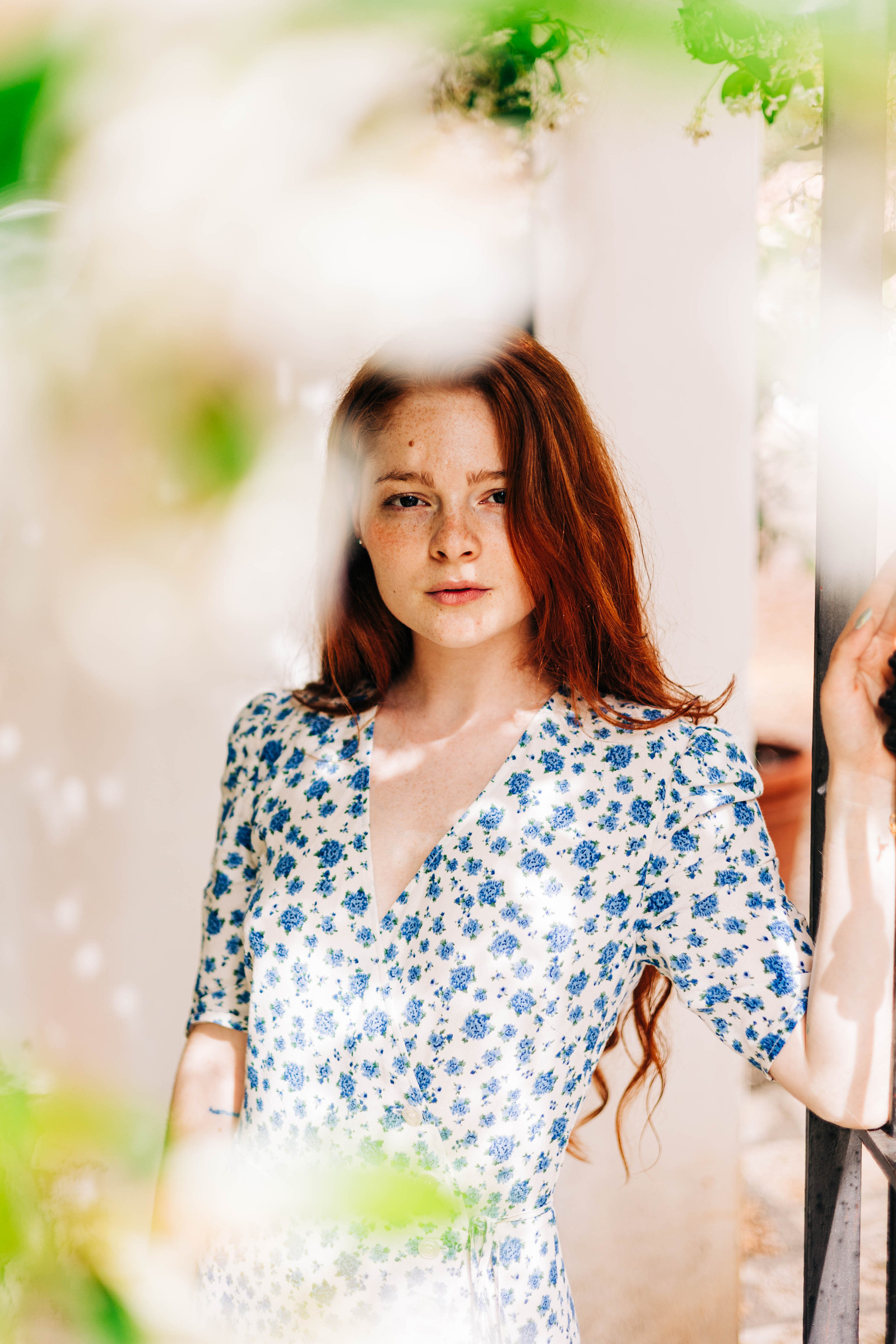 Model wearing a blue and white floral dress with red hair posing in the gardens of an Italian villa for a fashion editorial photoshoot