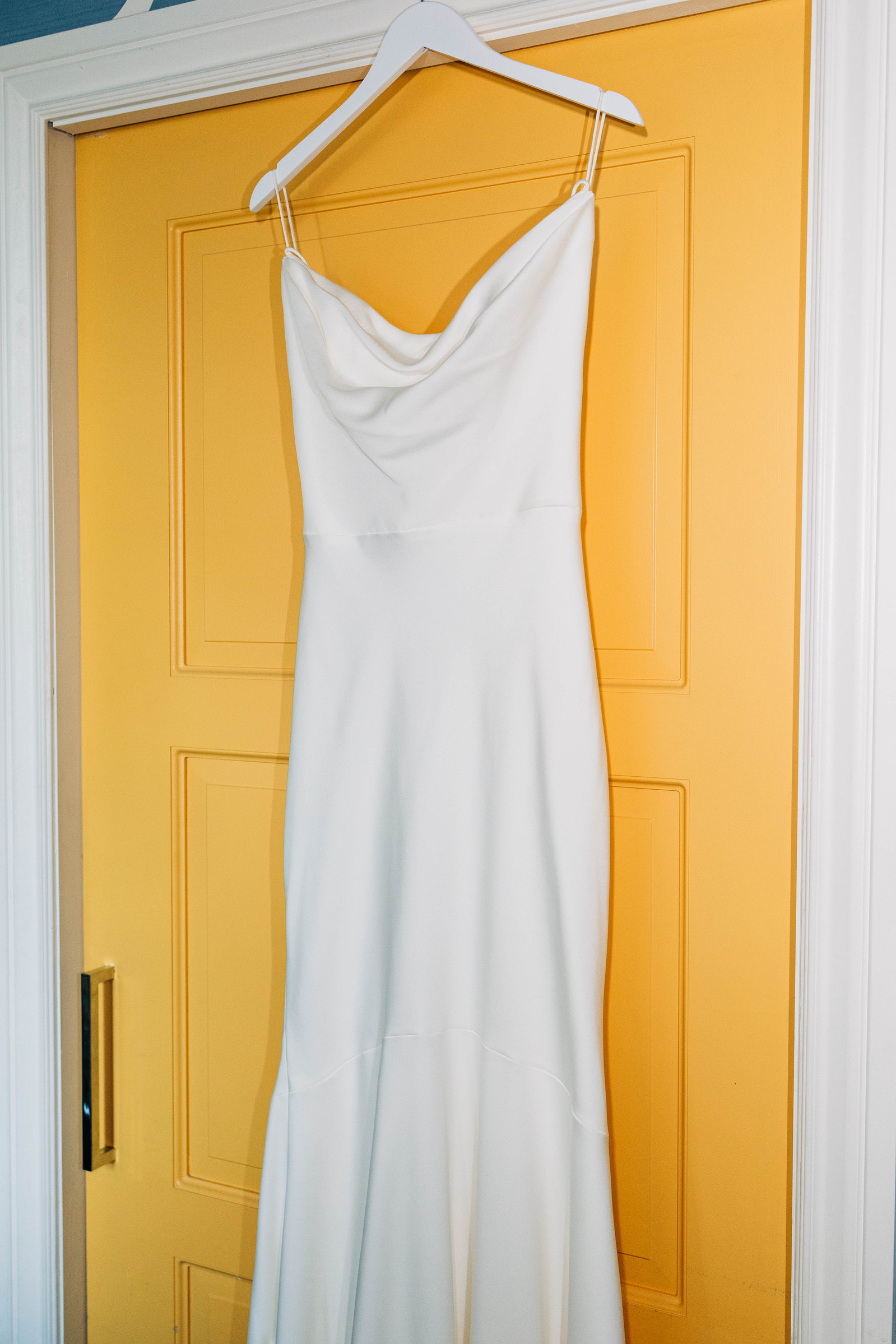 bright flash photography of simple elegant wedding dress by lovely bride philly hanging by yellow door at hotel monaco in old city