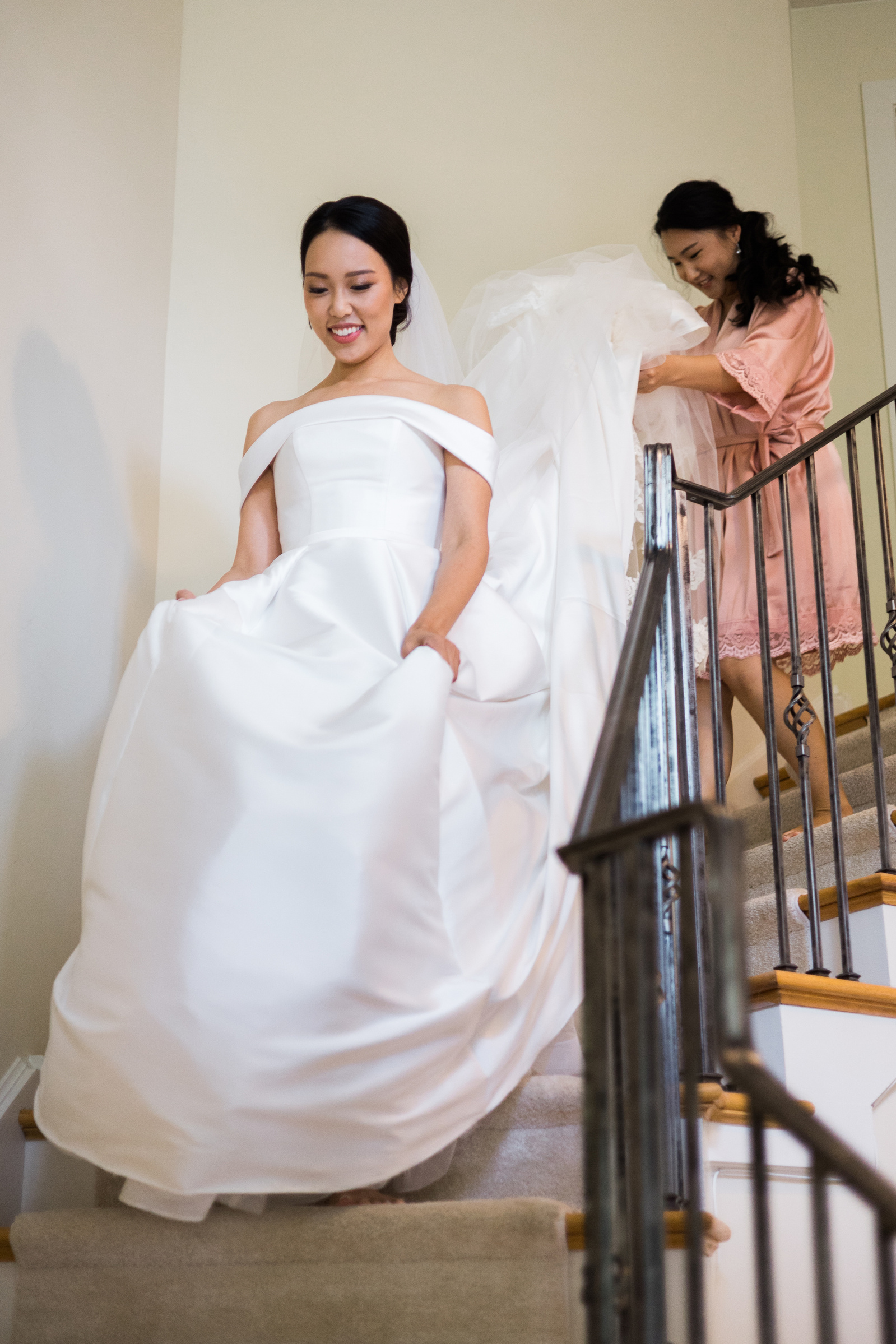 bridesmaid helping bride down the stairs in her wedding gown