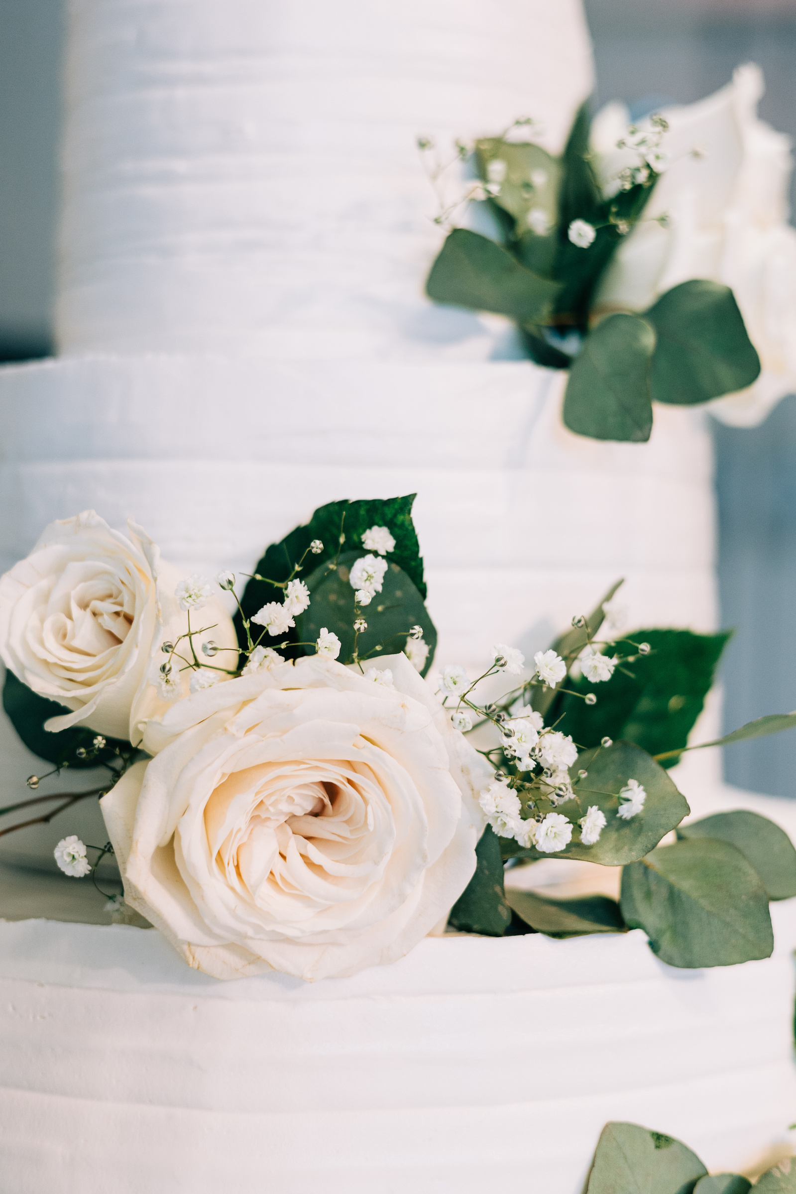 white tiered wedding cake with white roses and greenery