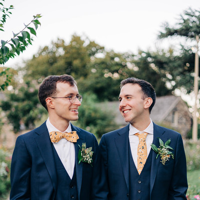 Two grooms smiling and holding hands on their wedding day at Bartram's Garden in Philadelphia LGBTQ Wedding Photographer