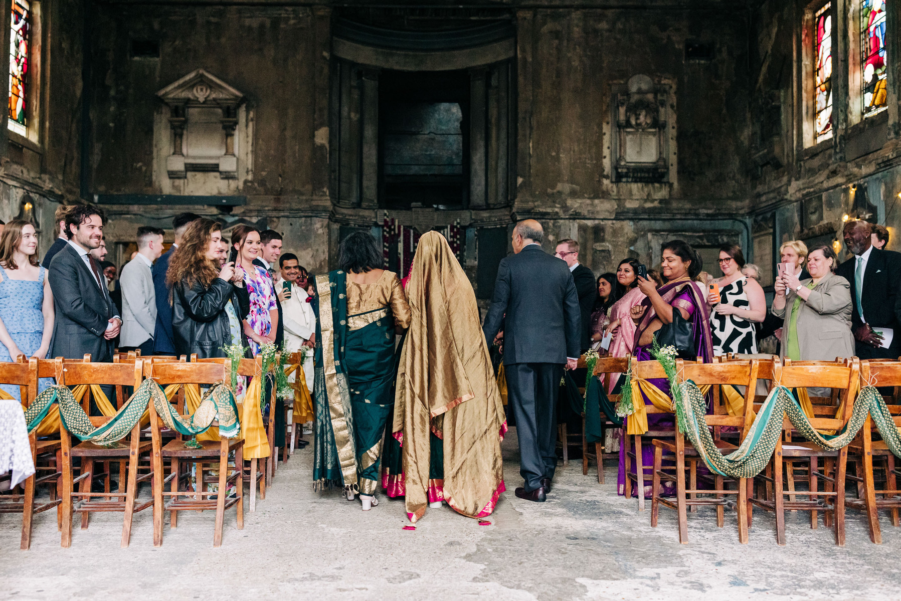 colorful multicultural british indian wedding at asylum chapel and amp studios in london england UK wedding bride walking down the aisle with her parents