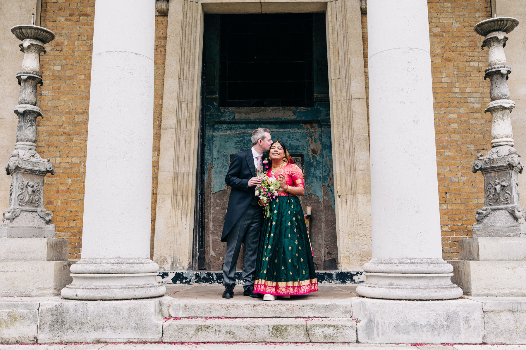 colorful multicultural british indian wedding at asylum chapel in london england UK wedding bride wearing hot pink and emerald green sari from nalli silks groom wearing suit from moss bros