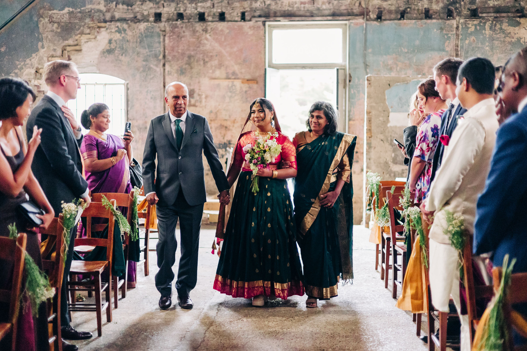 colorful multicultural british indian wedding at asylum chapel and amp studios in london england UK wedding bride walking down the aisle with her parents