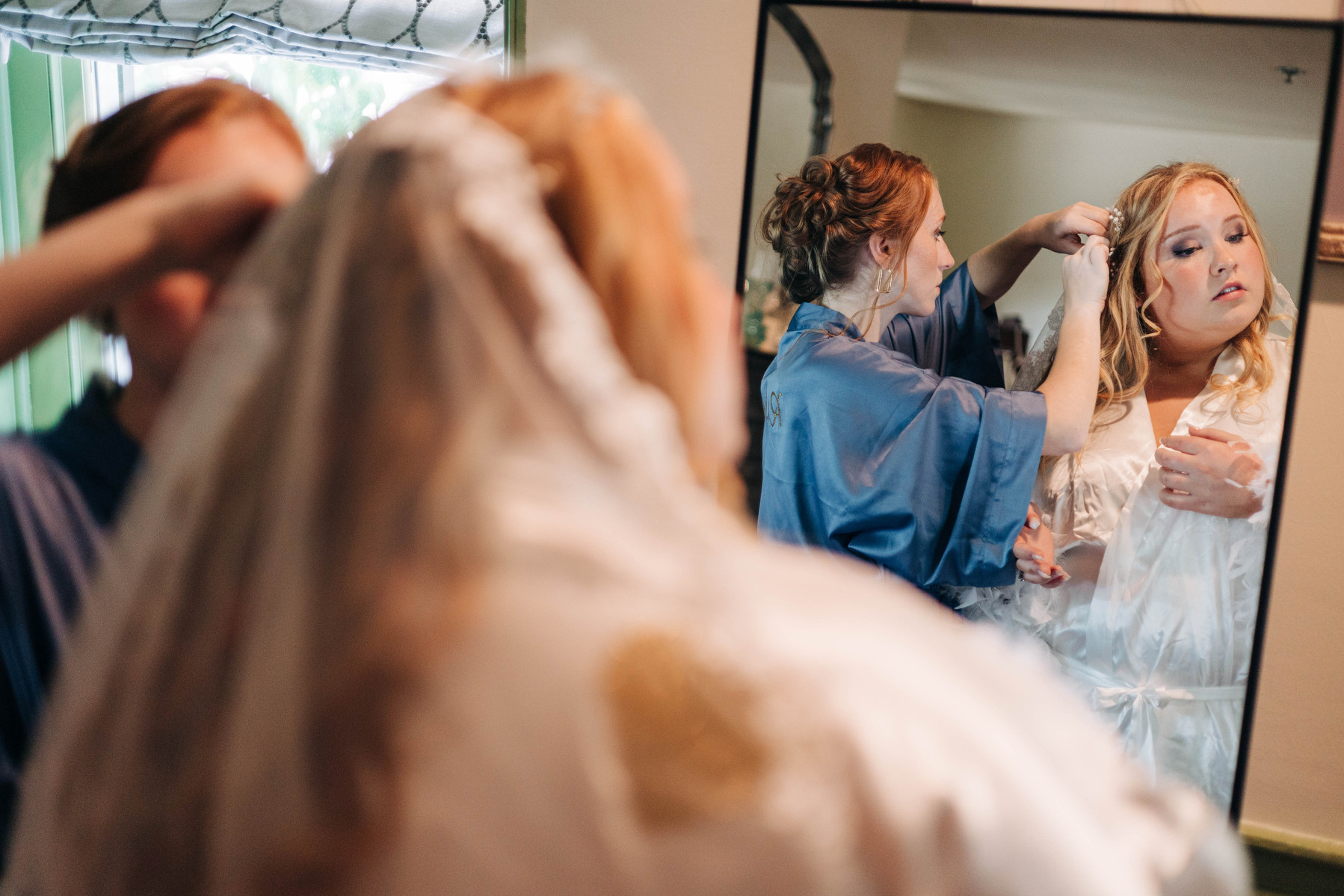 bride getting ready in mirror with birdesmaid on her wedding day 