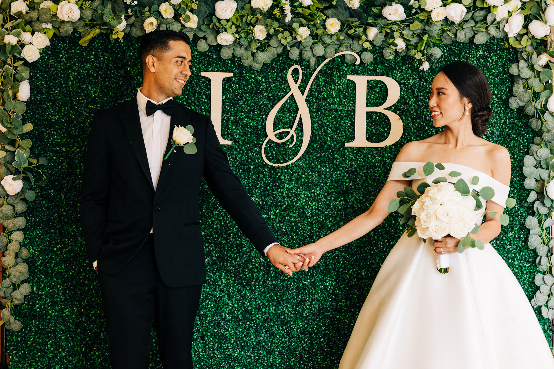 bride and groom hold hands in front of a flower wall on their wedding day 