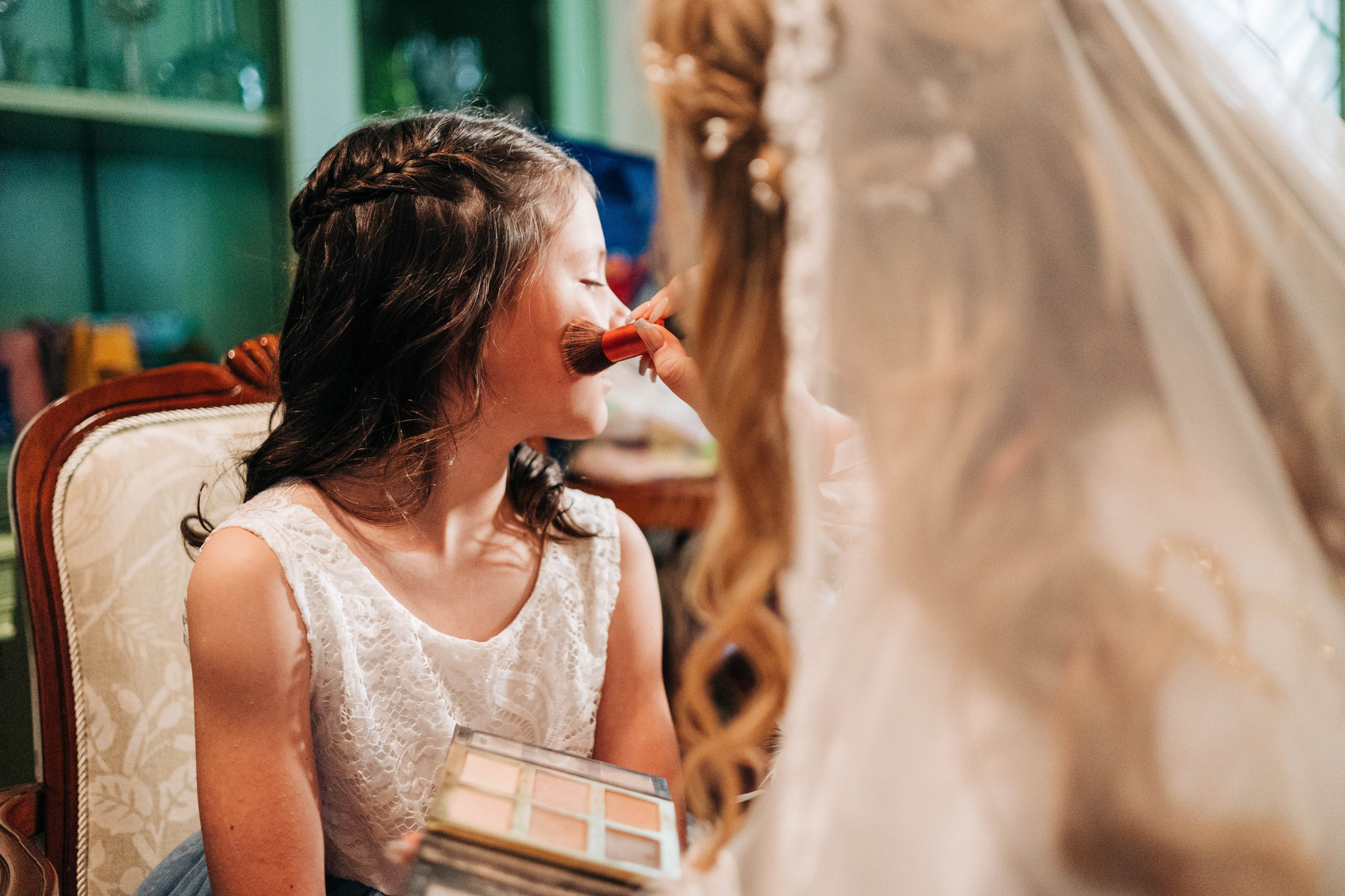 bride getting ready on wedding day doing flower girls makeup in bridal suite