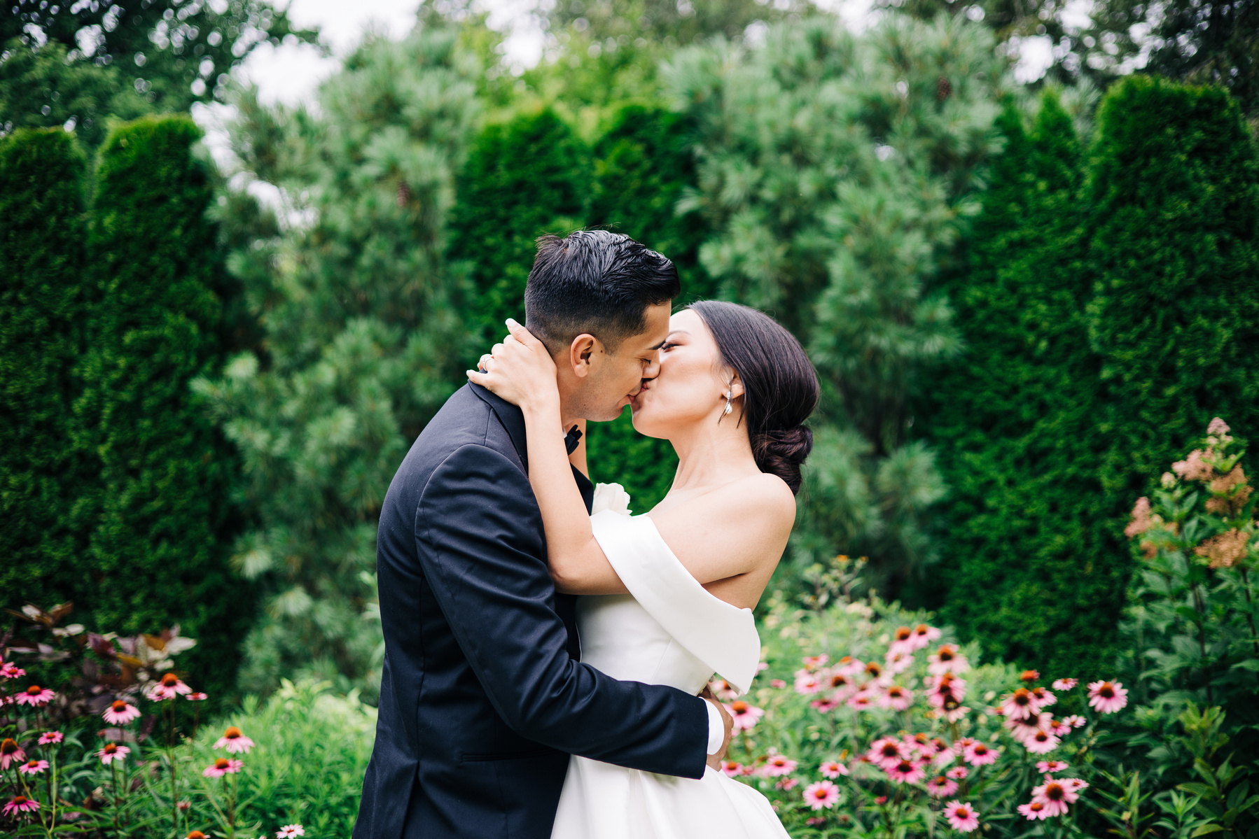 bride and groom kissing in a garden with pink flowers