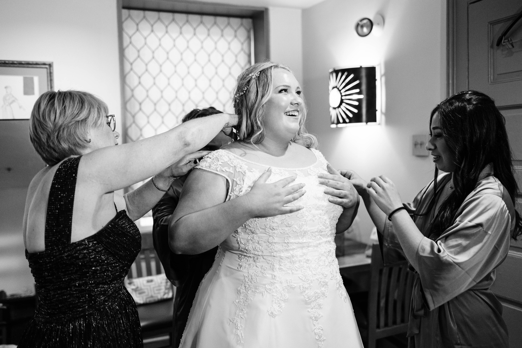 bride with bridesmaids and mom getting into her wedding dress