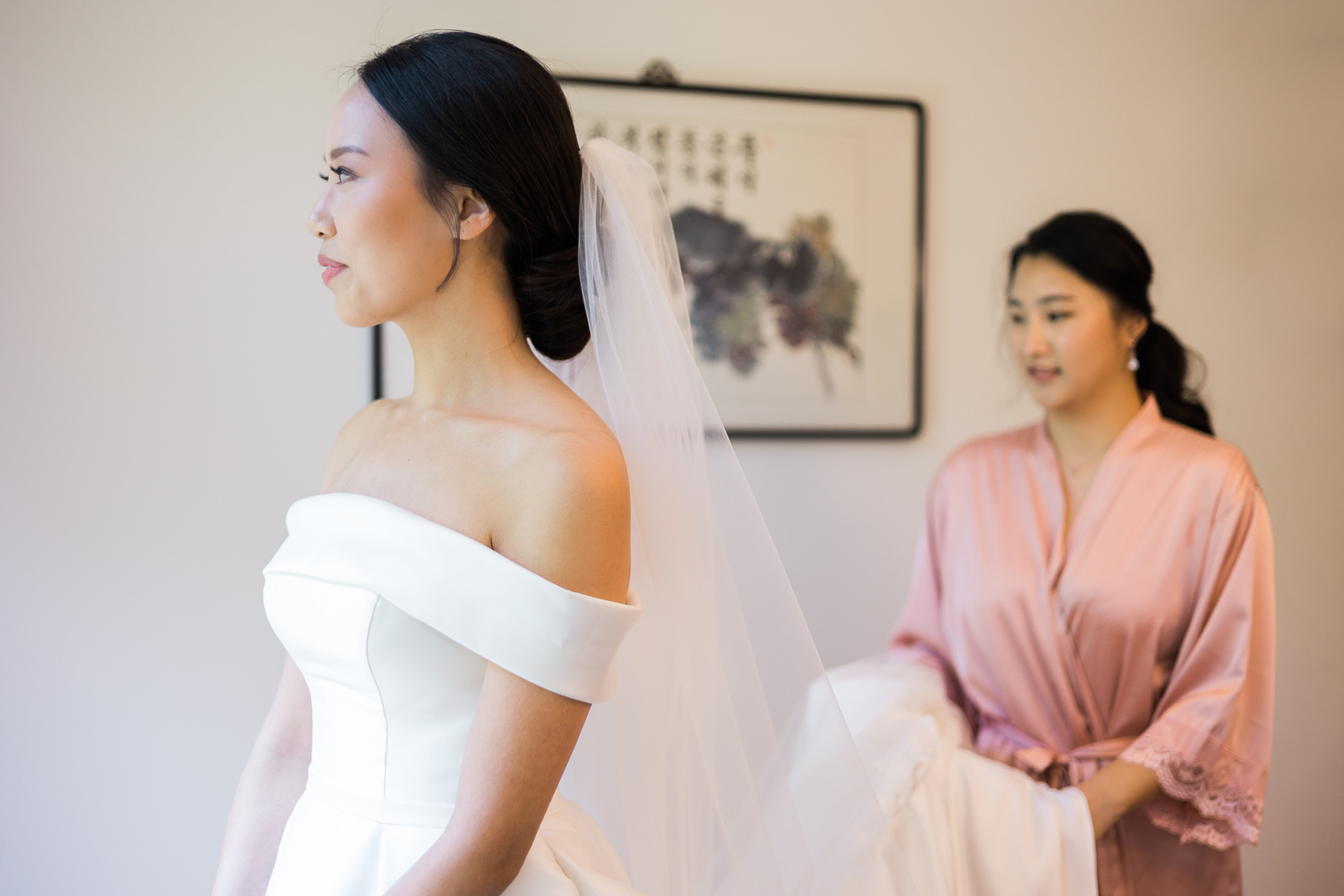 bridesmaid helping bride with her wedding gown as she prepares for the first look