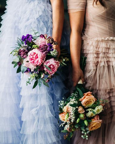 close up photo of two brides holding bouquets of flowers in bright pastel colors