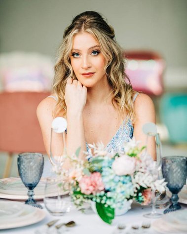 non-traditional bride poses at wedding table with bright pastel colors and blue wedding dress