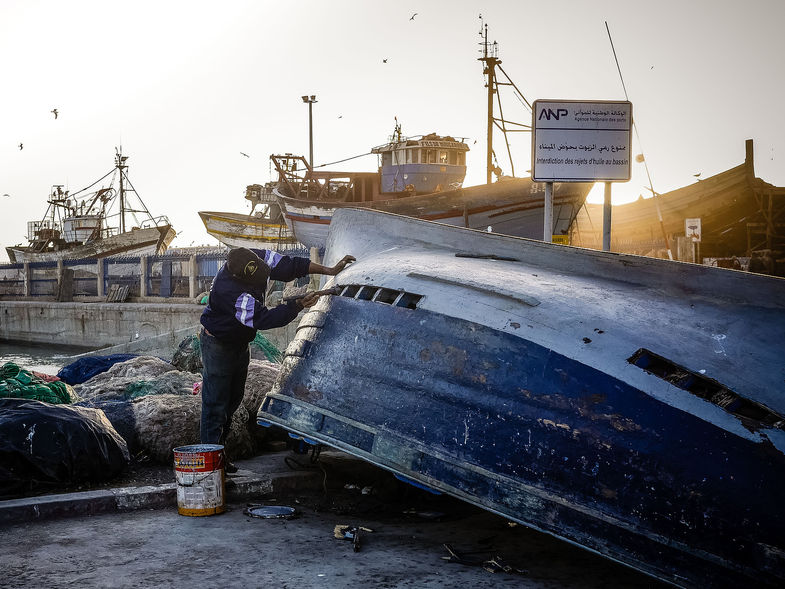 Un pêcheur repeint son bateau.