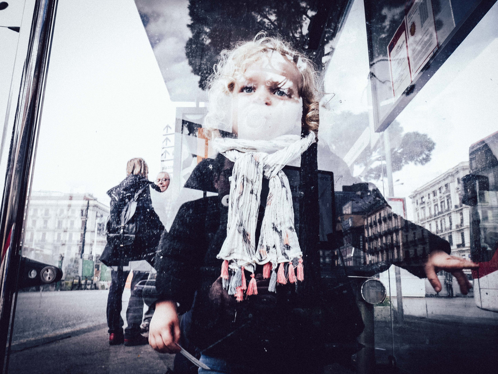 Une petite fille derrière une vitre qui a un reflet.