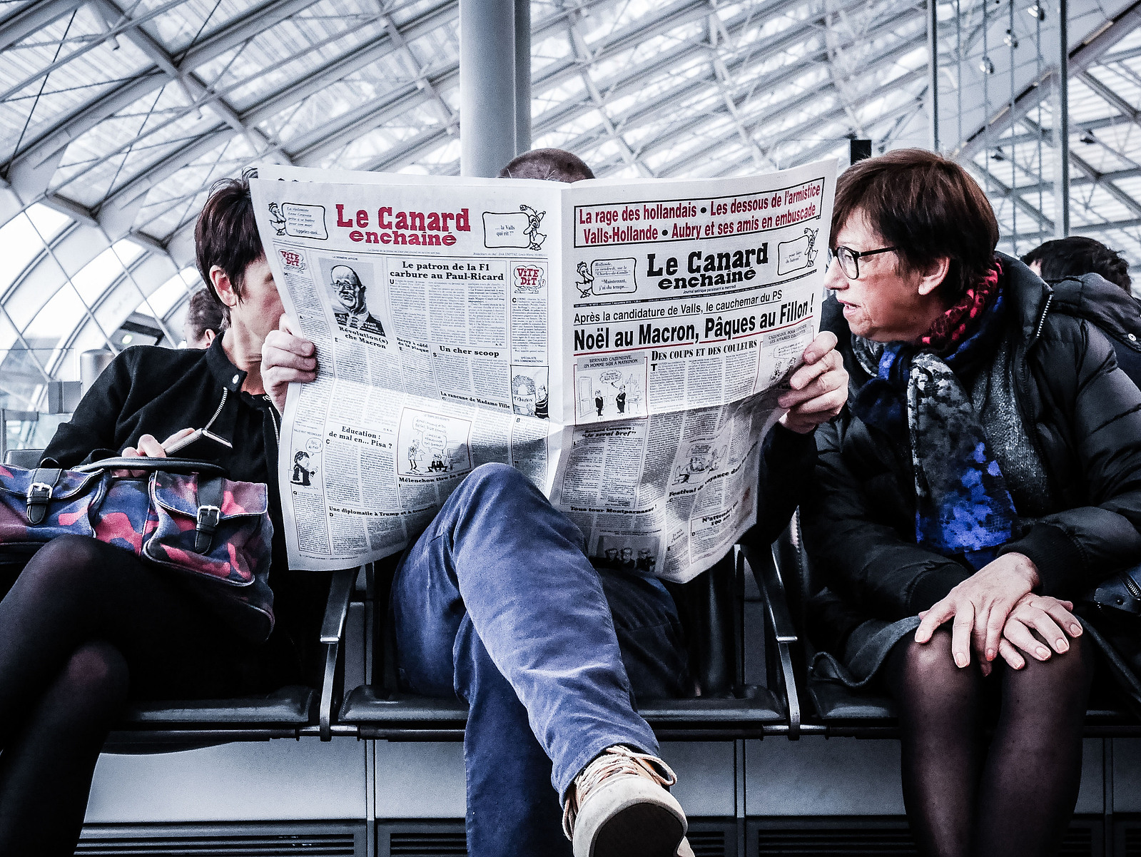 3 personnes qui lisent un journal dans un aéroport.