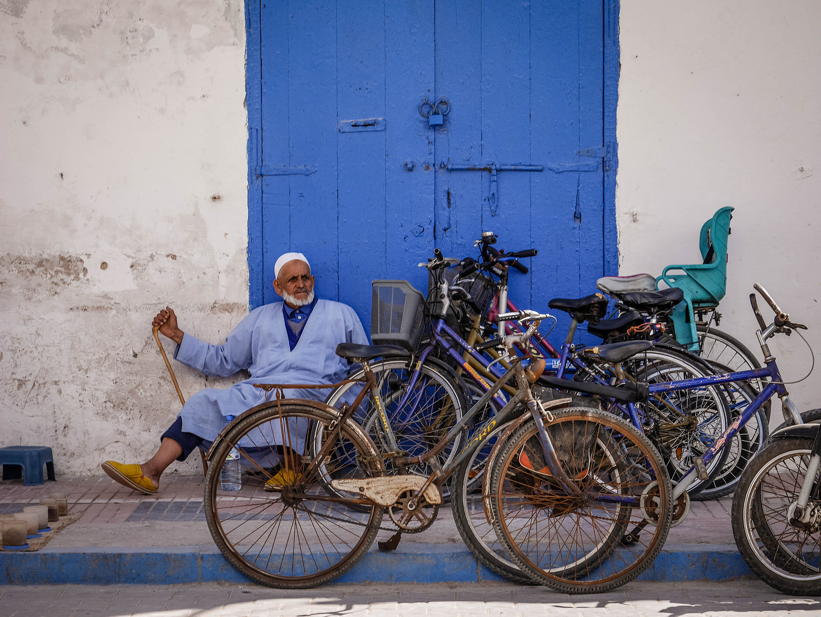 Un homme vieux avec une canne se repose sur des marches devant des vélos.