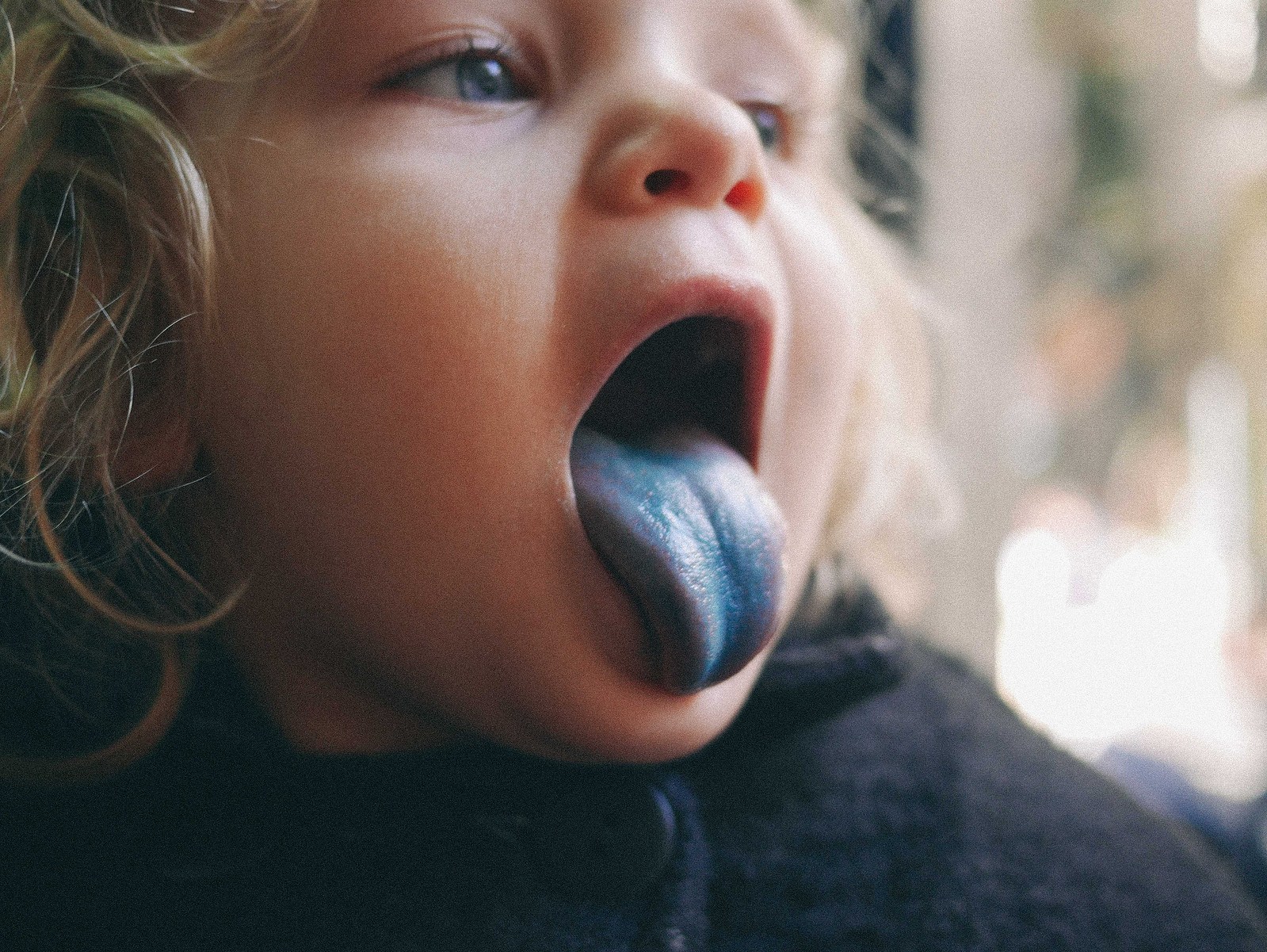 Une petite fille qui a mangé un bonbon à la langue toute bleue.