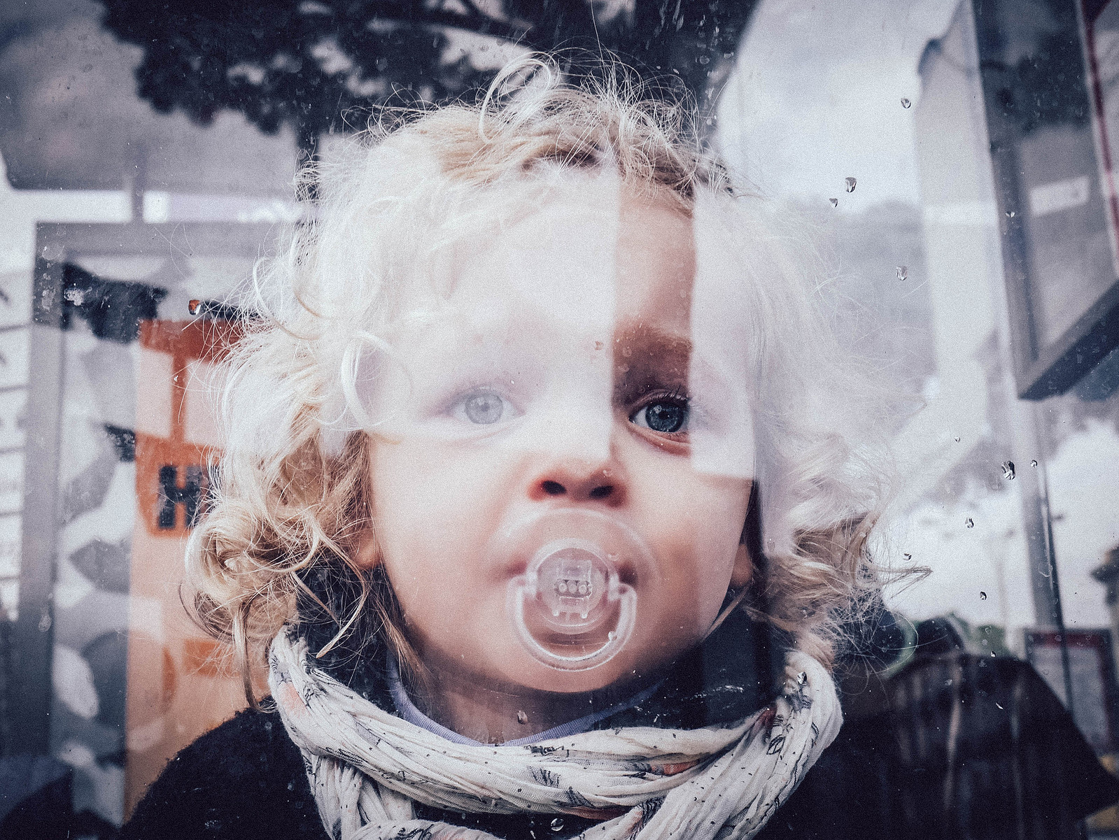 Une petite fille derrière une vitre qui a un reflet.