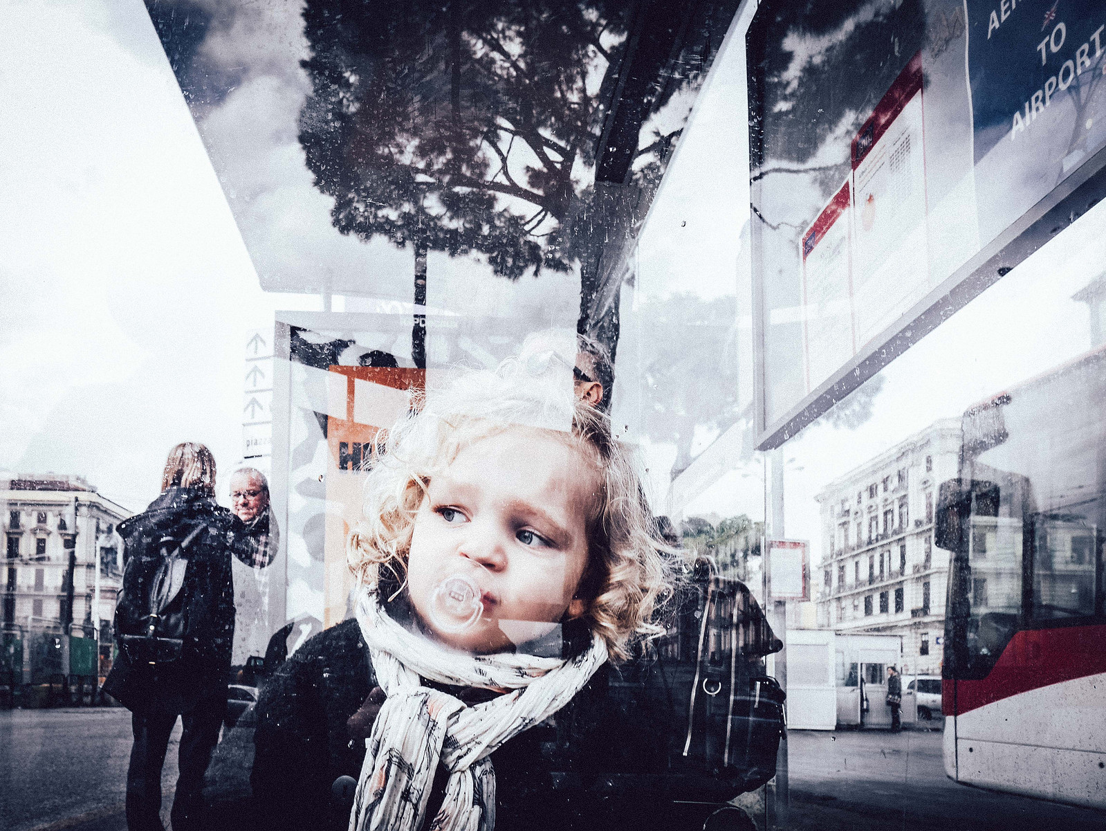 Une petite fille derrière une vitre qui a un reflet.