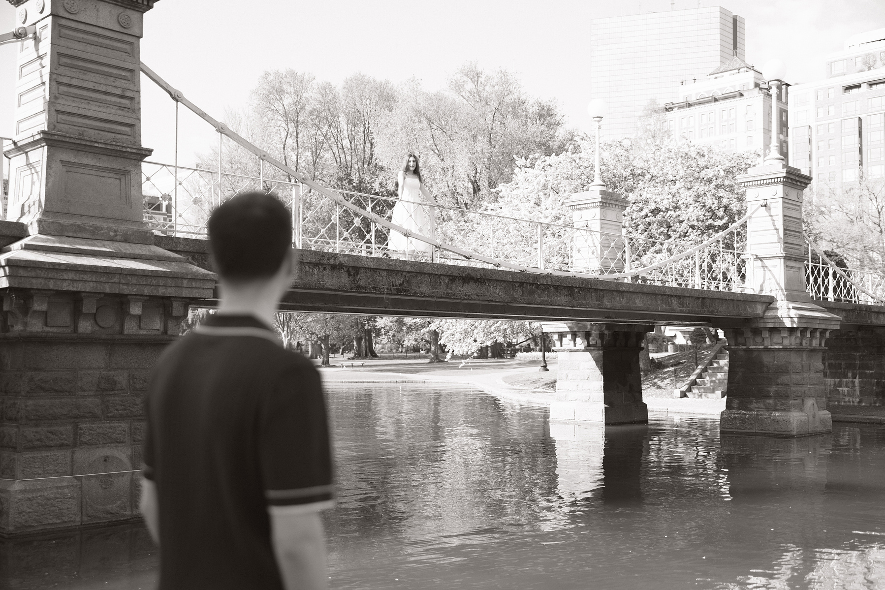 Bride overlooking the pond in Boston Commons, groom looking up at her. 