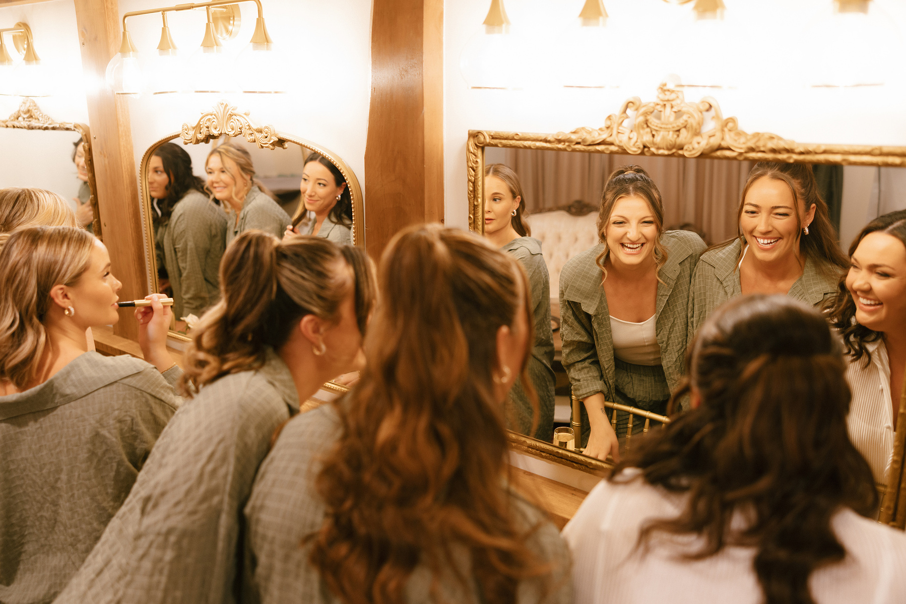 Bridesmaids are holding up champagne glasses and cheering in front of the mirror. 