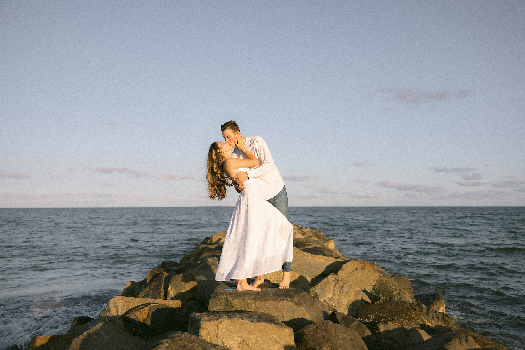 Bride and groom swooning over eachother on the rocks at the beach going in for a dip kiss. 