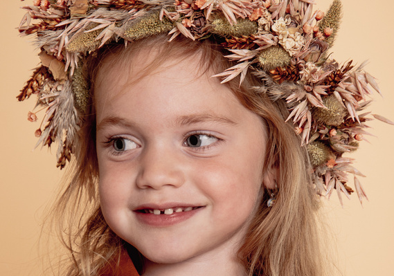 vrolijke blik met zongedroogde bloemen op haar hoofd, ondeugendheid in een chique jasje, speelse foto die zou kunnen gebruikt worden voor feestelijkheden zoals communie, kerst, nieuwjaar.