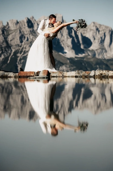 Ein Brautpaar küsst sich am See der Kaiserlounge in Tirol. Im Hintergrund sieht man den Wilden Kaiser. Brautpaarshooting - Hochzeitsfotografie - Tirol